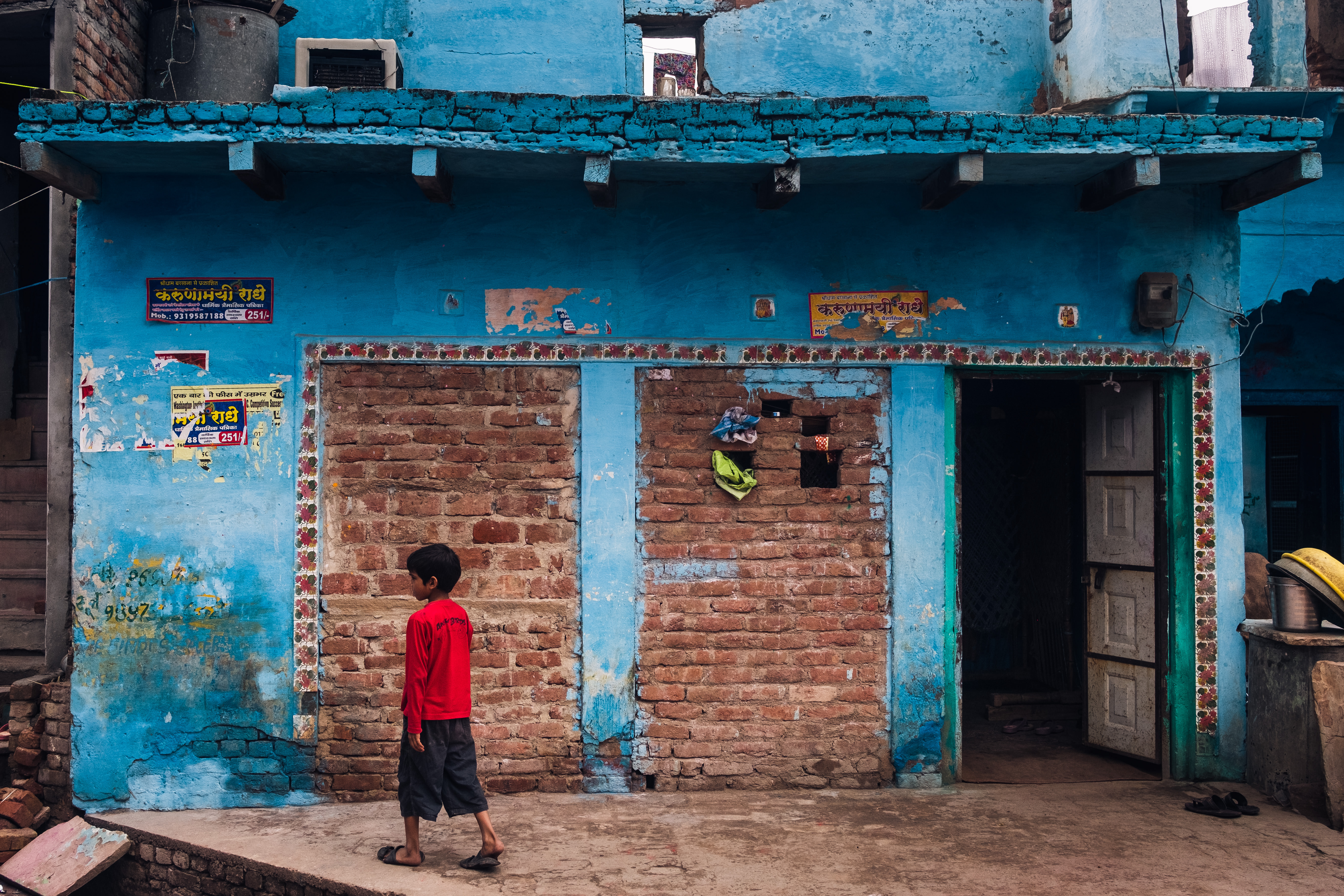 India Street Photography During Holi Festival. Boy in red walks in front of blue wall. Images by Jason Vinson