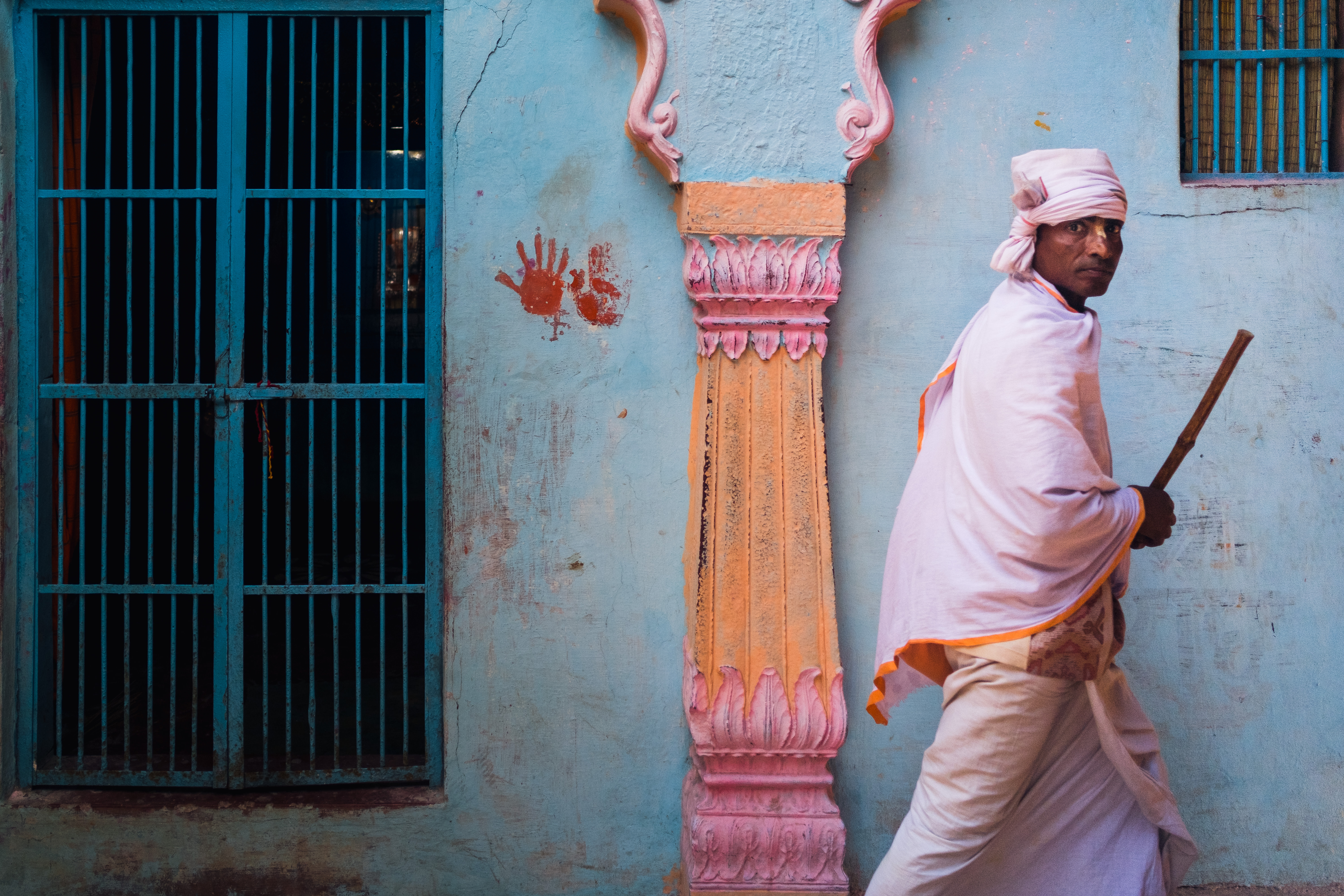 India Street Photography During Holi Festival. Man passes red hands on a blue wall. Images by Jason Vinson