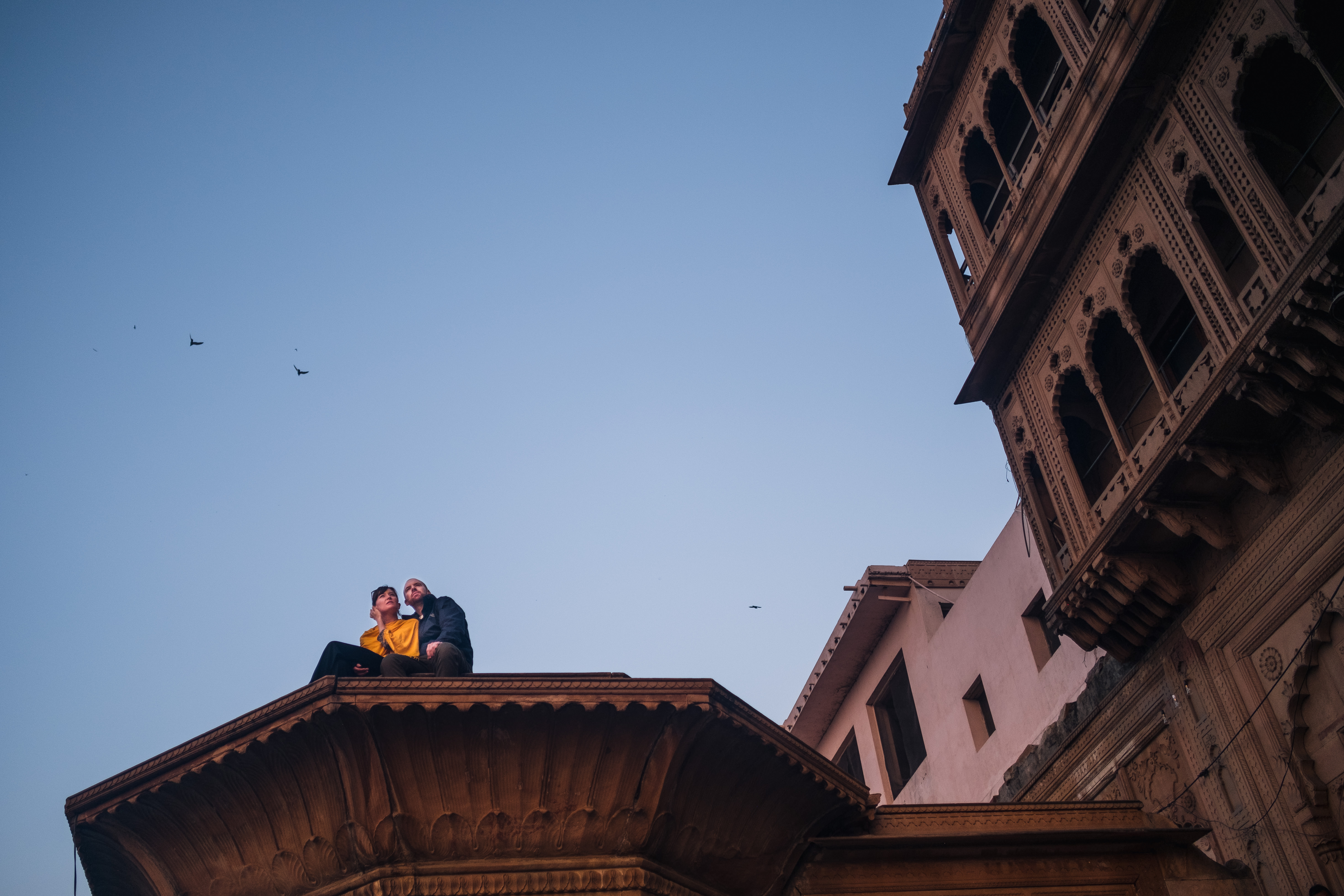 India Street Photography During Holi Festival. couple sits on a pillar and watches the festival. Images by Jason Vinson
