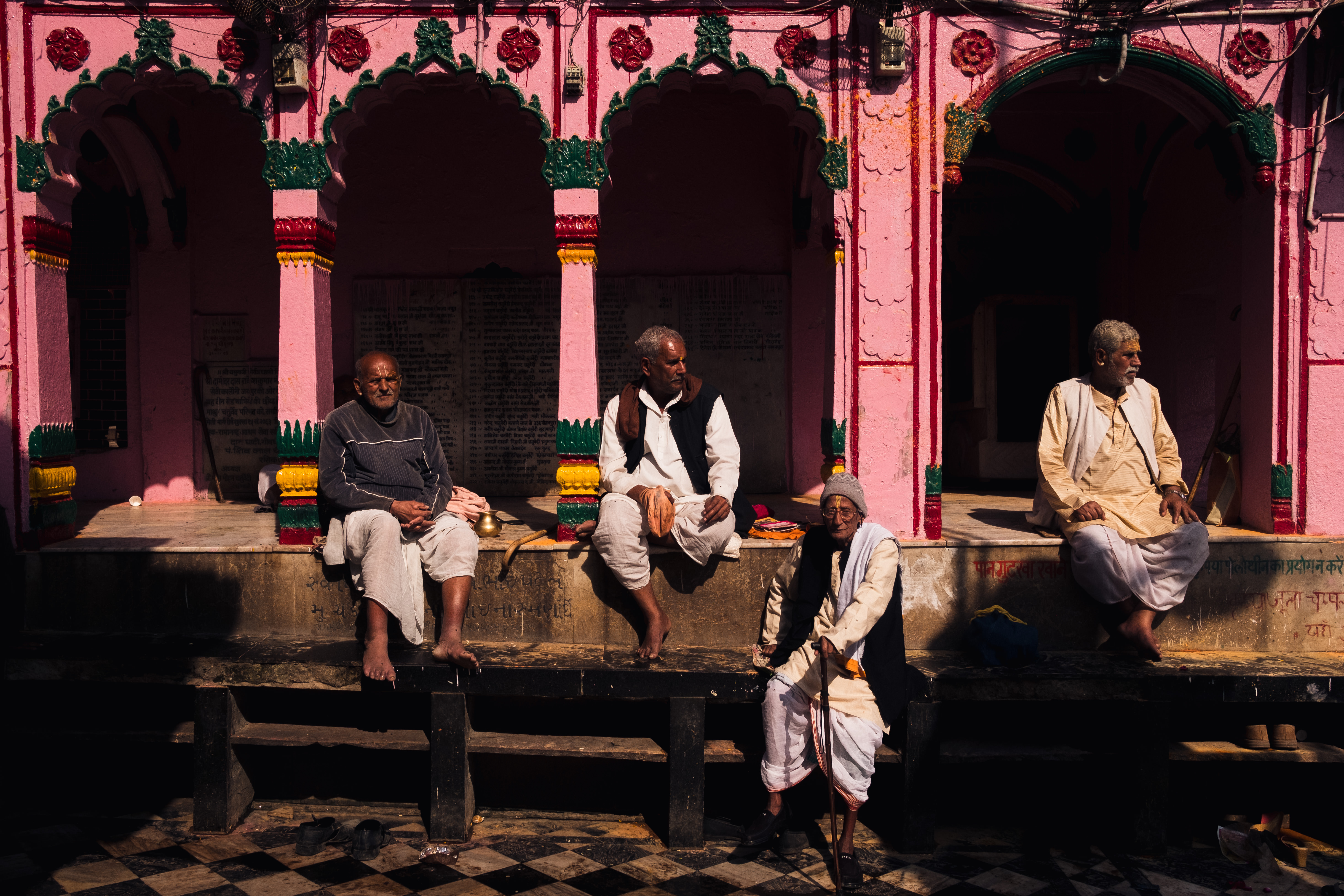 India Street Photography During Holi Festival. Men sitting and taking by pink wall. Images by Jason Vinson