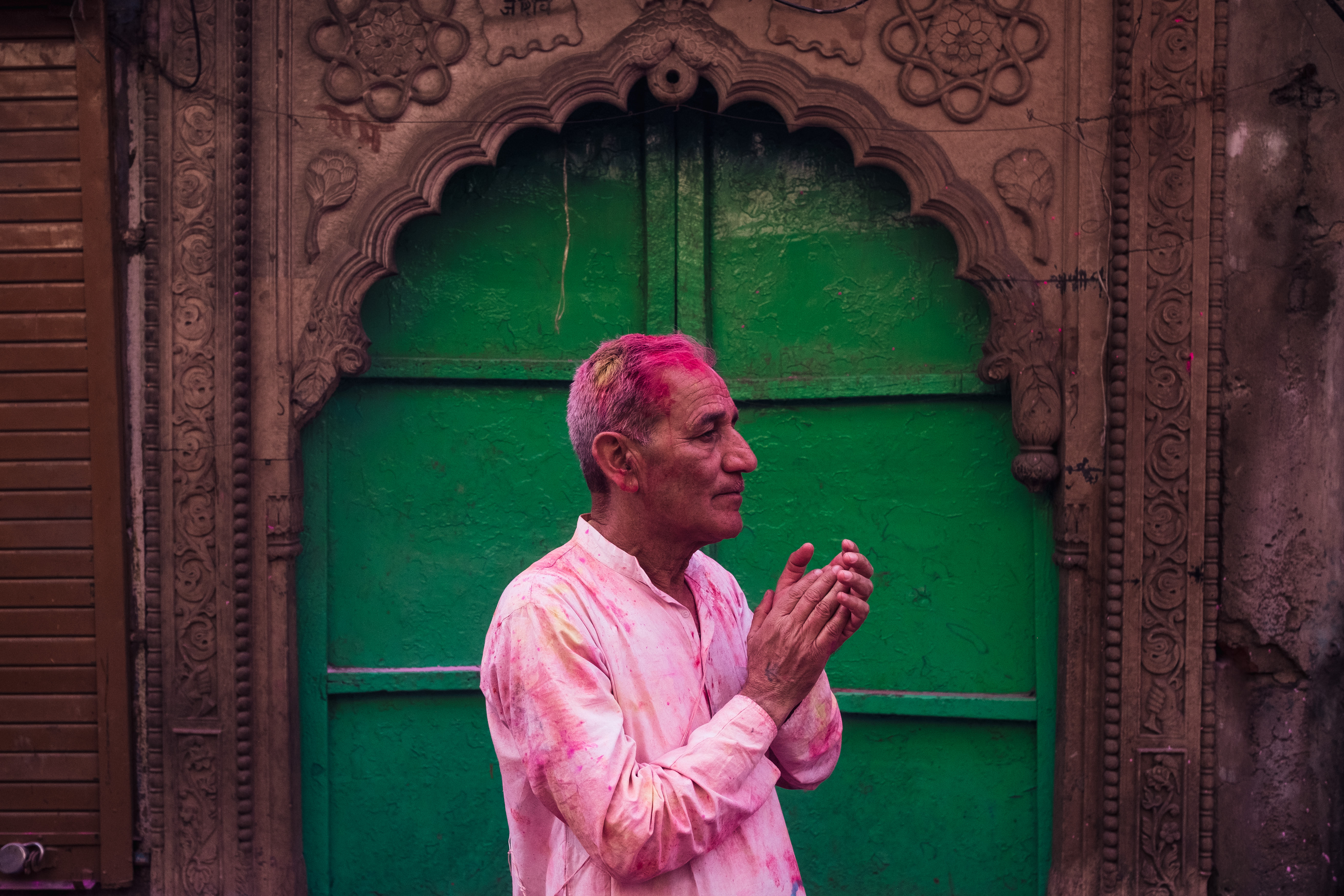 India Street Photography During Holi Festival. man covered in pink stand in front of green door. Images by Jason Vinson