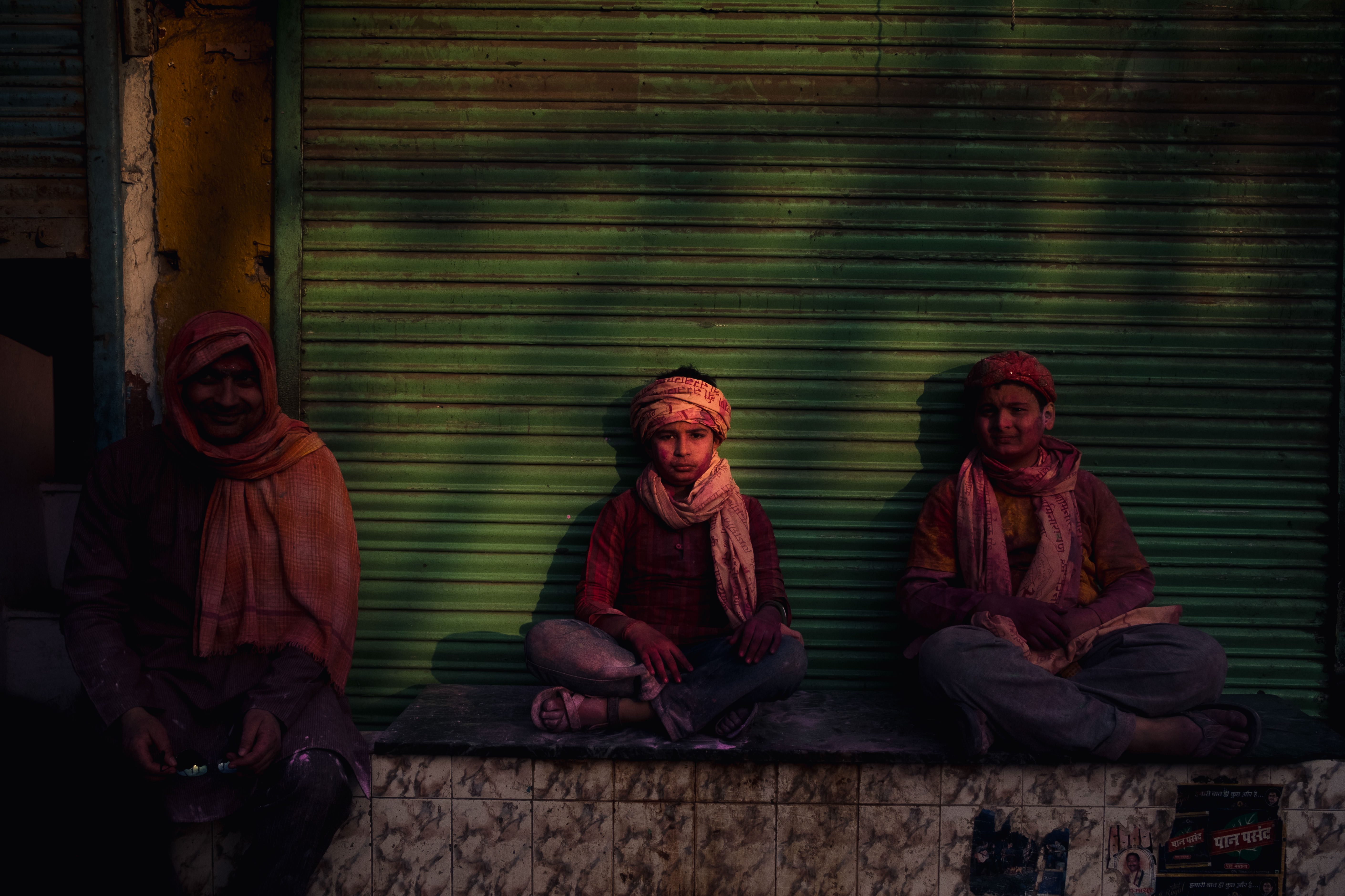 India Street Photography During Holi Festival. boy sits on sunlight in front of green door. Images by Jason Vinson