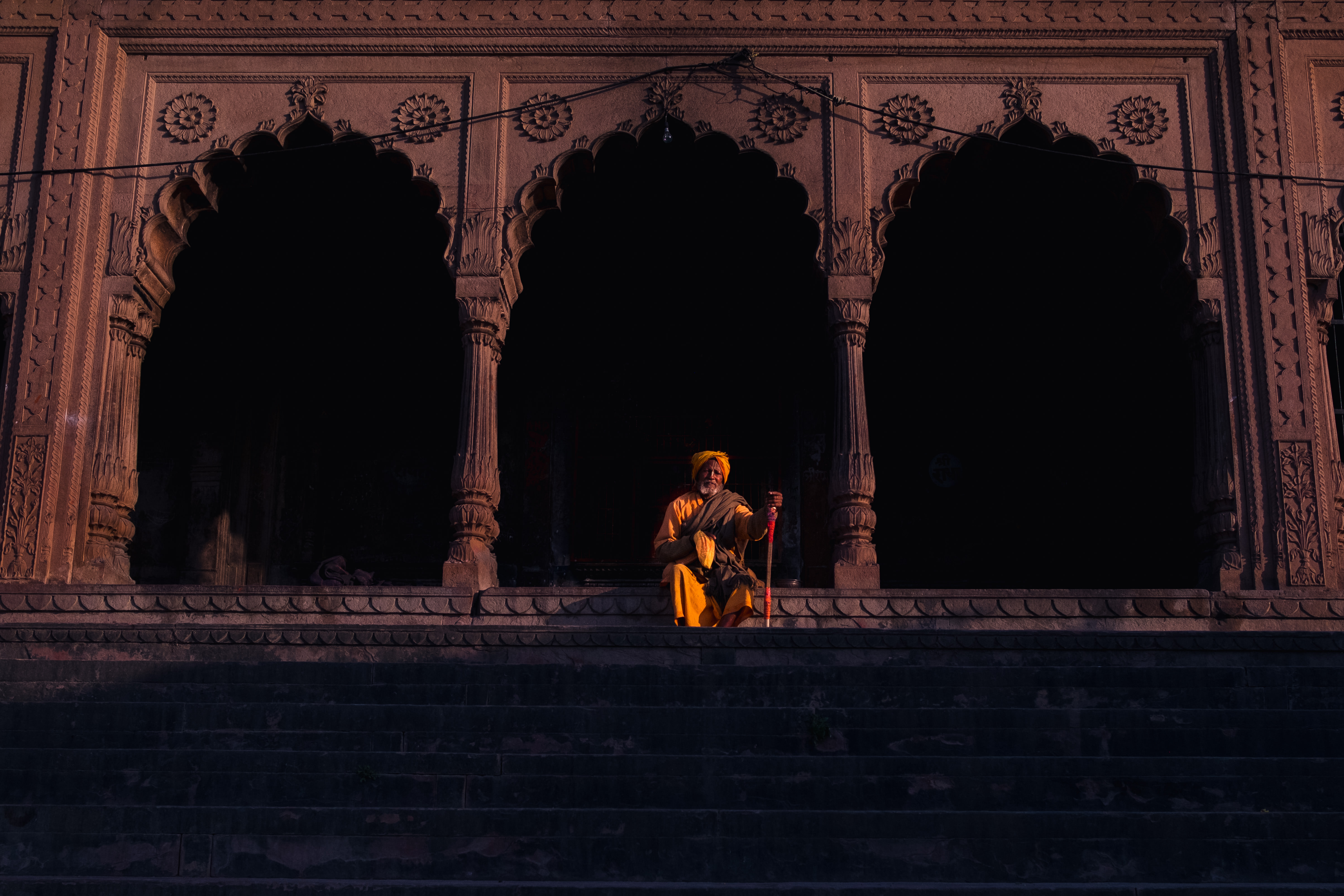 India Street Photography During Holi Festival. lone priest sits among the light. Images by Jason Vinson