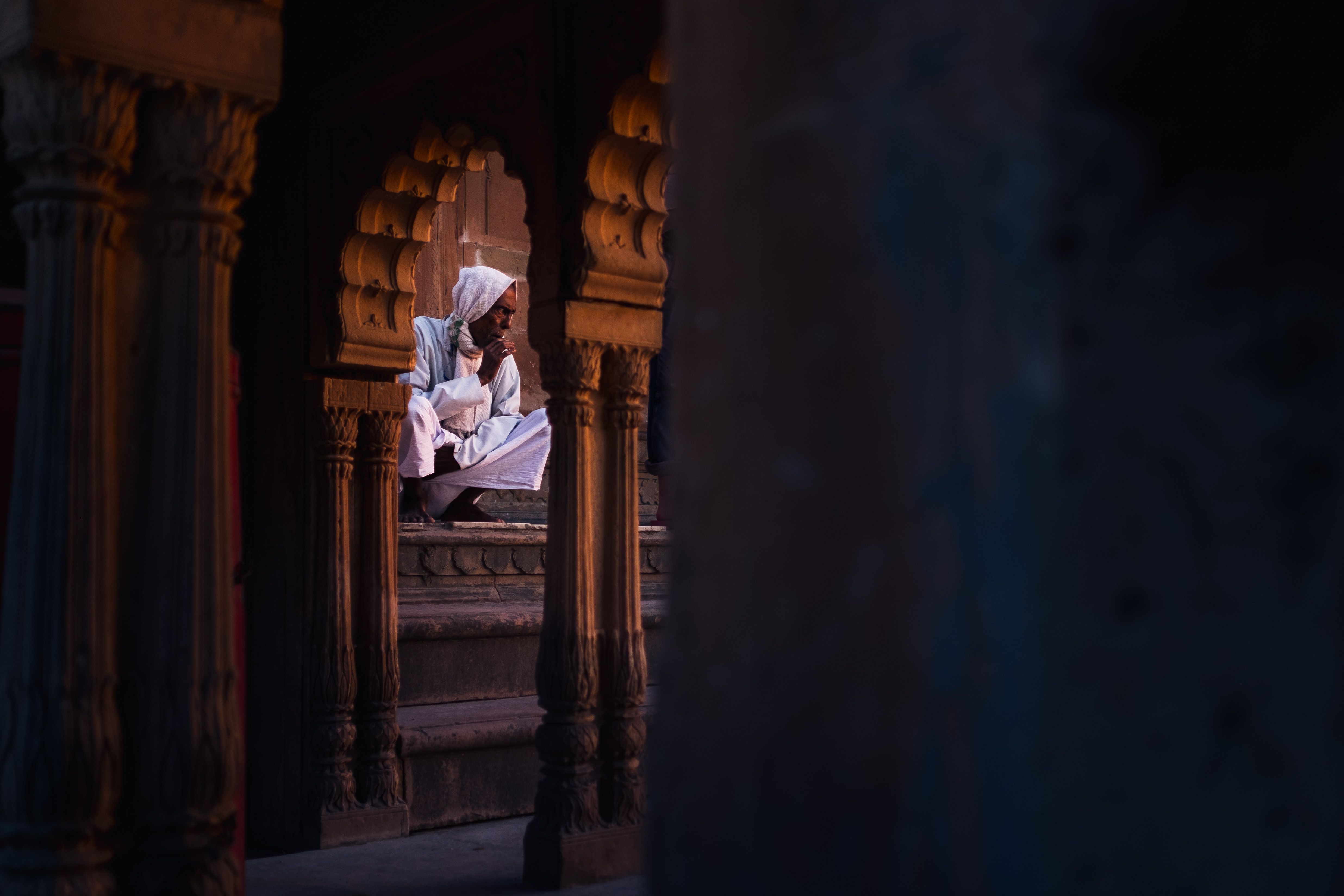 India Street Photography During Holi Festival. Priest sits on the stairs as people celebrate . Images by Jason Vinson