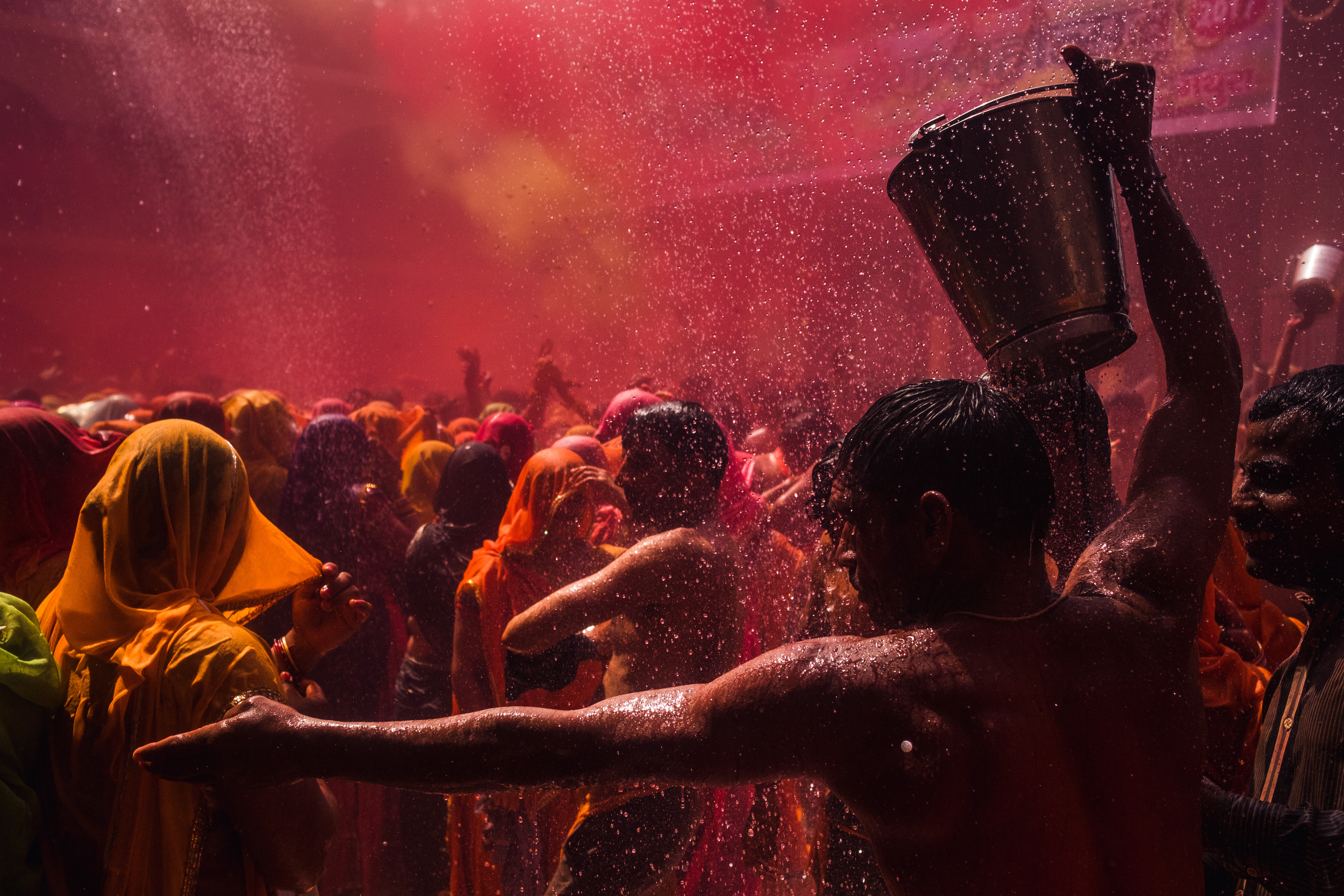India Street Photography During Holi Festival. man gestures to people as he fills his bucket with water. Images by Jason Vinson
