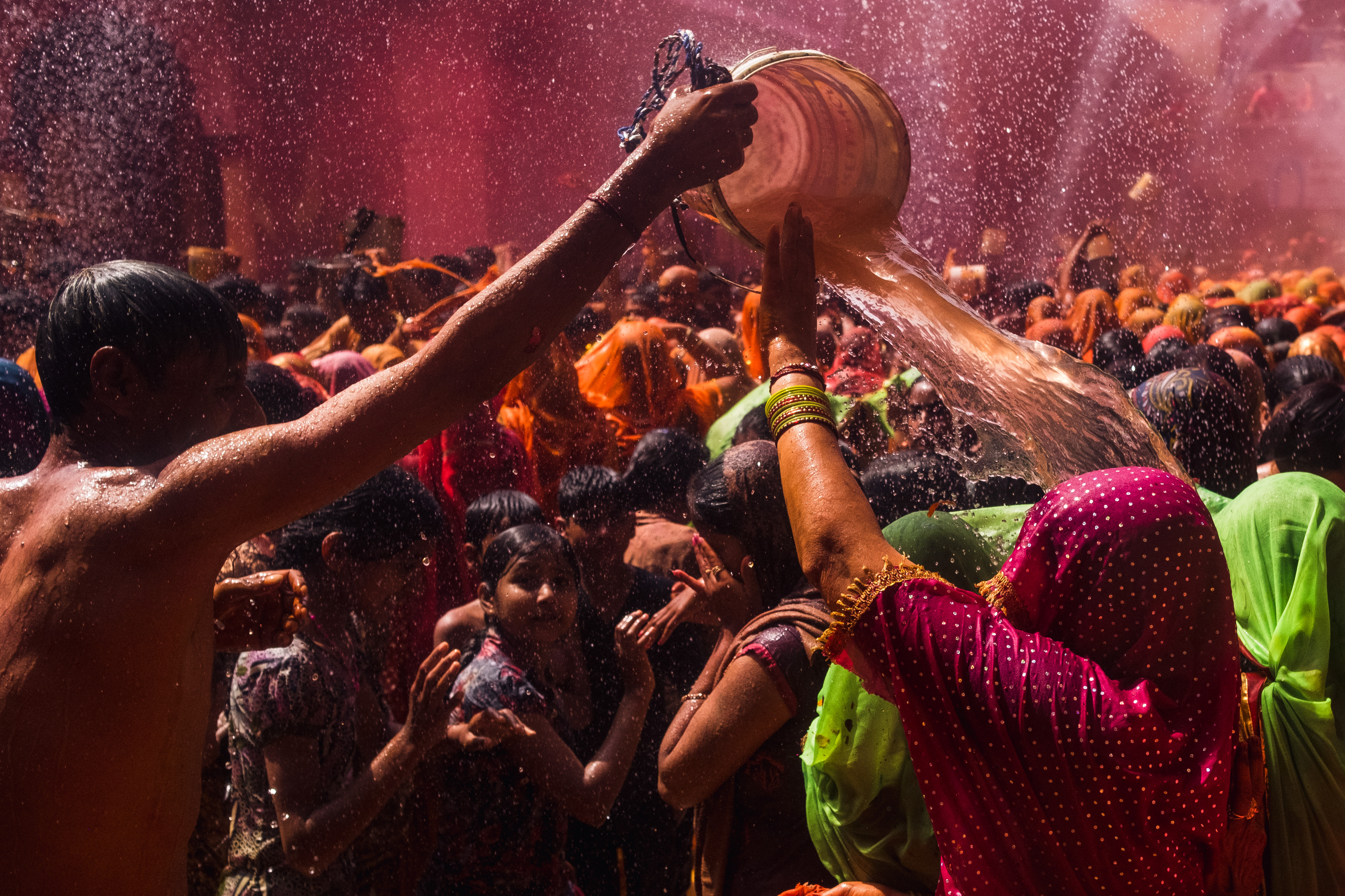 India Street Photography During Holi Festival. man throws bucket of water on lady as she tries to stop the water. Images by Jason Vinson