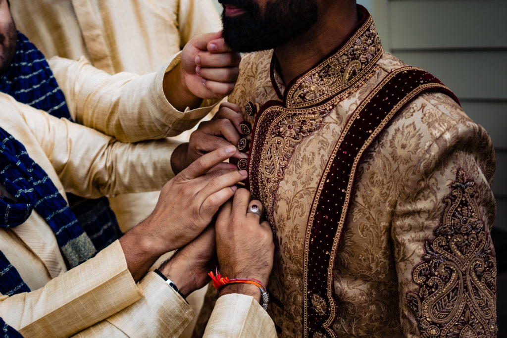 Northwest Arkansas Indian Wedding Photography Vinson Images- groom gets help with jacket as friend plays with his beard