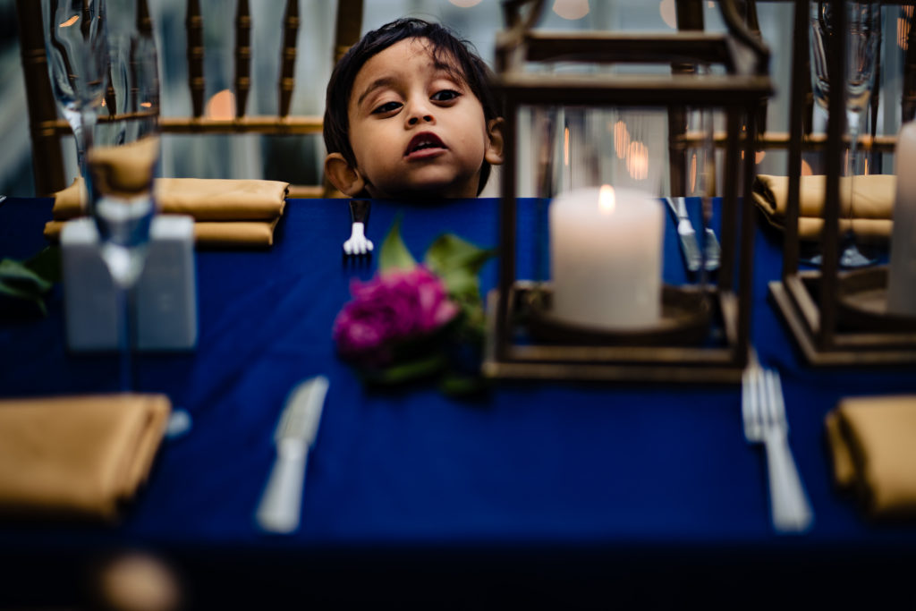 Northwest Arkansas Indian Wedding Photography Vinson Images- boy peeks over table looking for food 