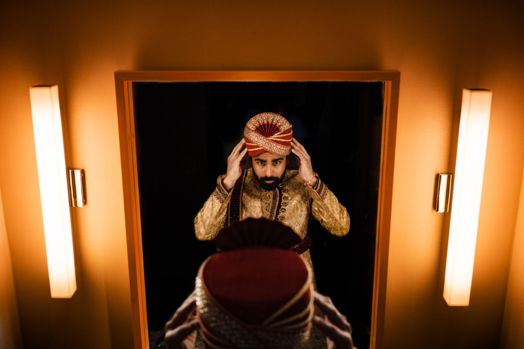 Northwest Arkansas Indian Wedding Photography Vinson Images- groom adjusting his turban in front of a mirror  