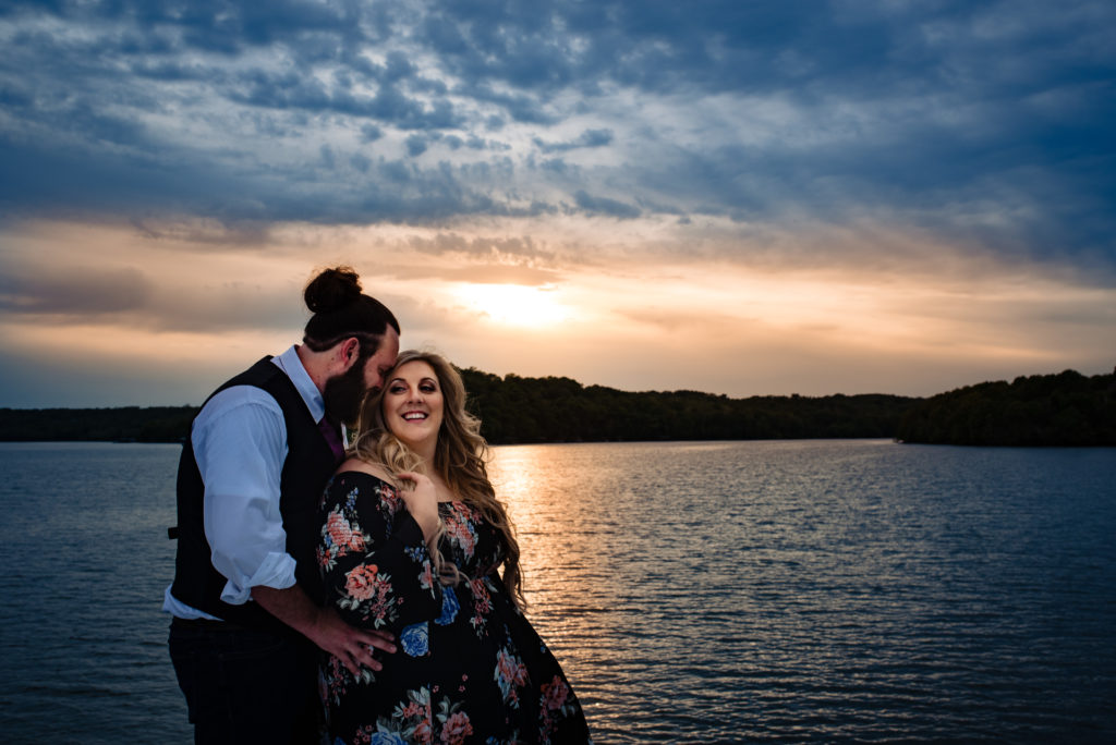 Northwest Arkansas Wedding Photography - Vinson Images - Beaver lake Engagement -  couple cuddling with shoreline and sunset