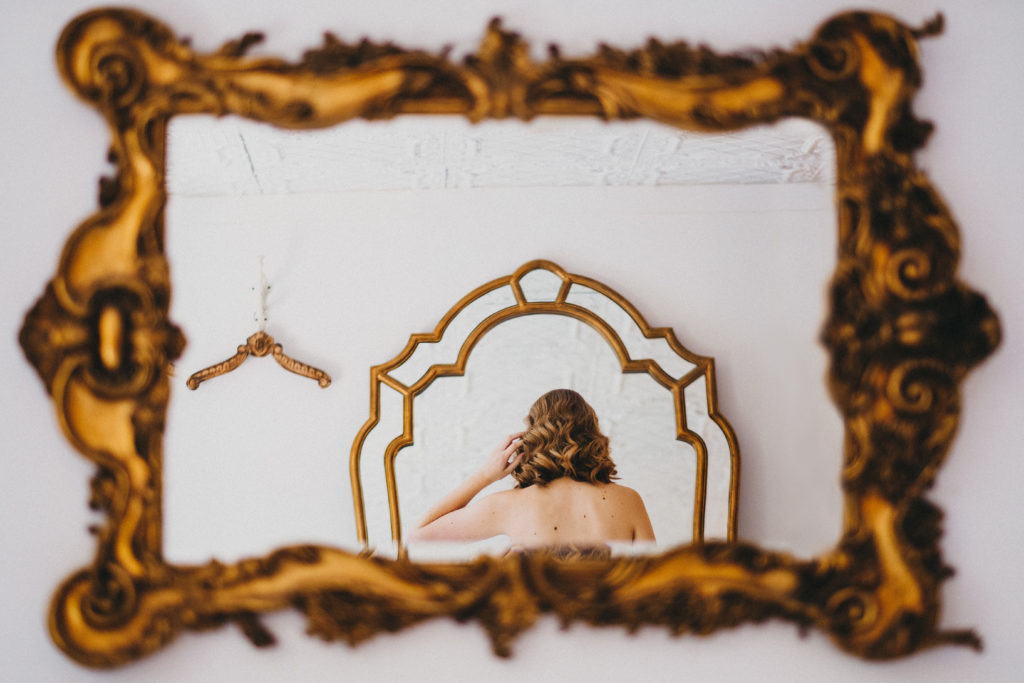 Bride looks through gold framed mirror 